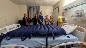 L’équipe du 4ᵉ étage pose avec le nouveau matelas de transfert MaxiAir installé sur un lit d’hôpital.
